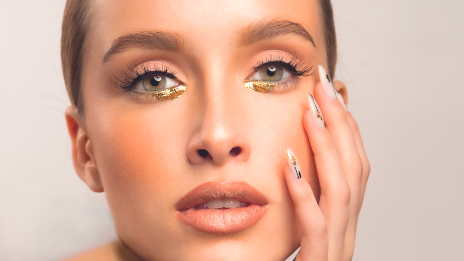 Una donna in primo piano che si tocca il viso, con gli occhi visibilmente truccati con l'oro e delle bellissime ciglia