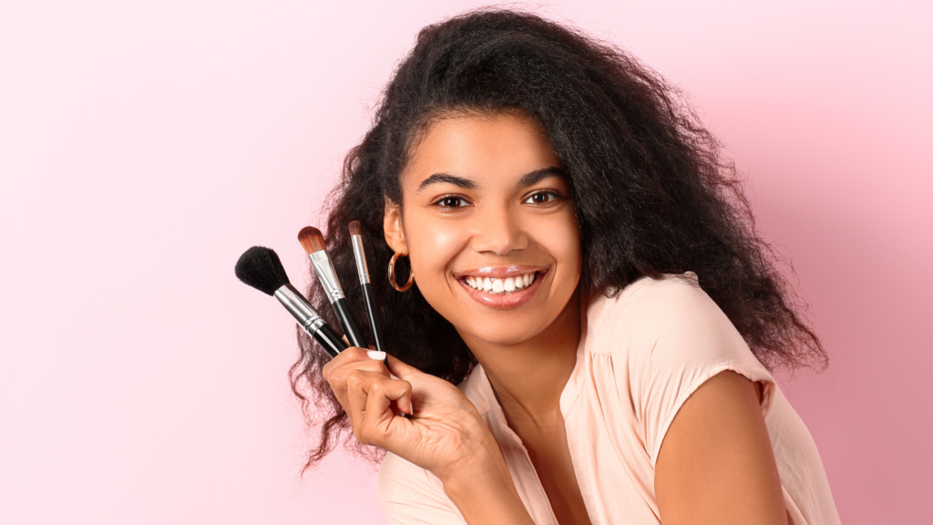 Primo piano del volto di una donna, che ha in manno dei pennelli da trucco. Una fot che rappresenta i temi di bellezza, moda ed eleganza, la fiera estetica Innovation Beauty Lab.