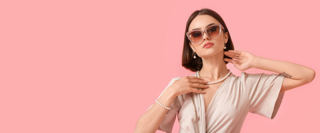 Ritratto di bella donna che indossa occhiali eleganti e gioielli su sfondo rosa, che rappresenta la fiera estetica Innovation Beauty Lab.