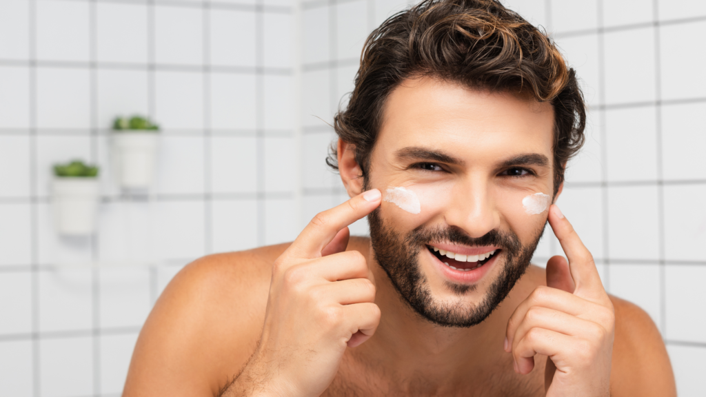 in foto è rappresentato un uomo in bagno, che si applica una crema per il viso. L'immagine rappresenta l'universo uomo nel beauty, in particolare la cosmesi per uomo e i trattamenti a lui dedicati.