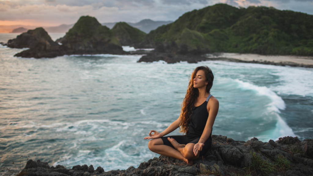 Giovane donna che pratica yoga nella posa del loto al tramonto con splendida vista sull'oceano e sulle montagne. significa sensibilità alla natura, autoanalisi e ricerca interiore. Concetto spirituale ed emotivo che riporta alle origini dell'evento corpo, mente e benessere organizzato da atar 22.
