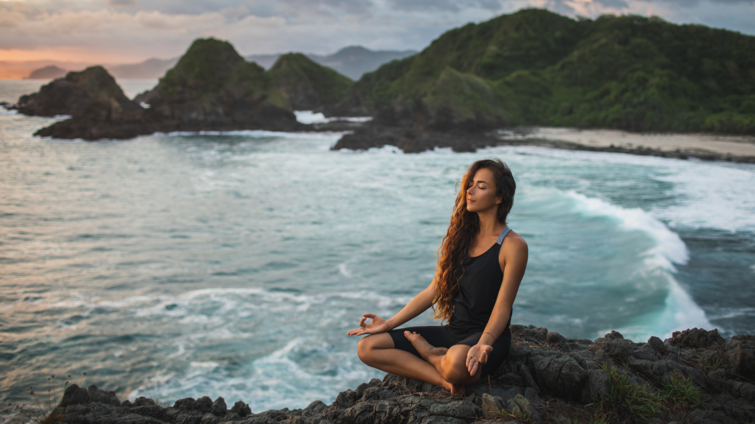 Giovane donna che pratica yoga nella posa del loto al tramonto con splendida vista sull'oceano e sulle montagne. significa sensibilità alla natura, autoanalisi e ricerca interiore. Concetto spirituale ed emotivo che riporta alle origini dell'evento corpo, mente e benessere organizzato da atar 22.