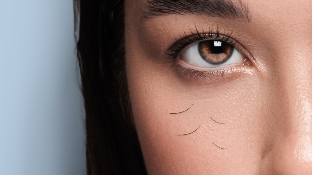 L'immagine mostra un primo piano dell'occhio di una donna con pelle liscia e ciglia ben definite. Sotto l'occhio, sulla guancia, sono visibili alcune ciglia cadute, evidenziando il problema della caduta delle ciglia. Lo sfondo è sfumato e chiaro, mettendo in risalto lo sguardo e il dettaglio delle ciglia perse. L'illuminazione morbida enfatizza la naturalezza della pelle e il focus dell'immagine.