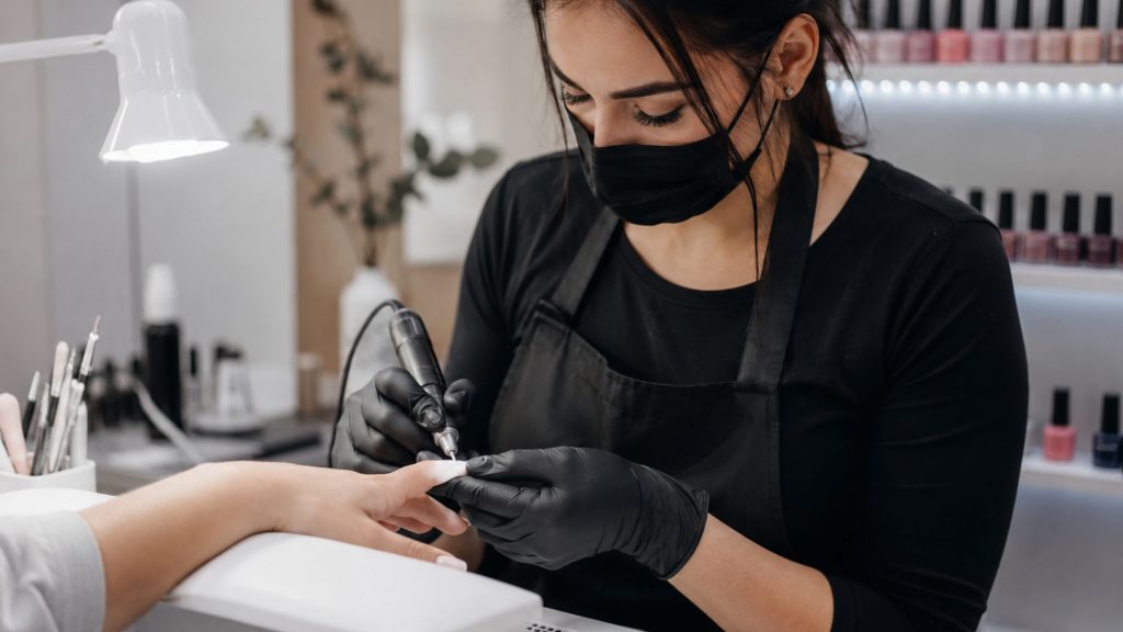 Onicotecnica al lavoro in un moderno centro estetico mentre esegue una ricostruzione unghie su una cliente, utilizzando strumenti professionali per la manicure in un ambiente luminoso e curato.