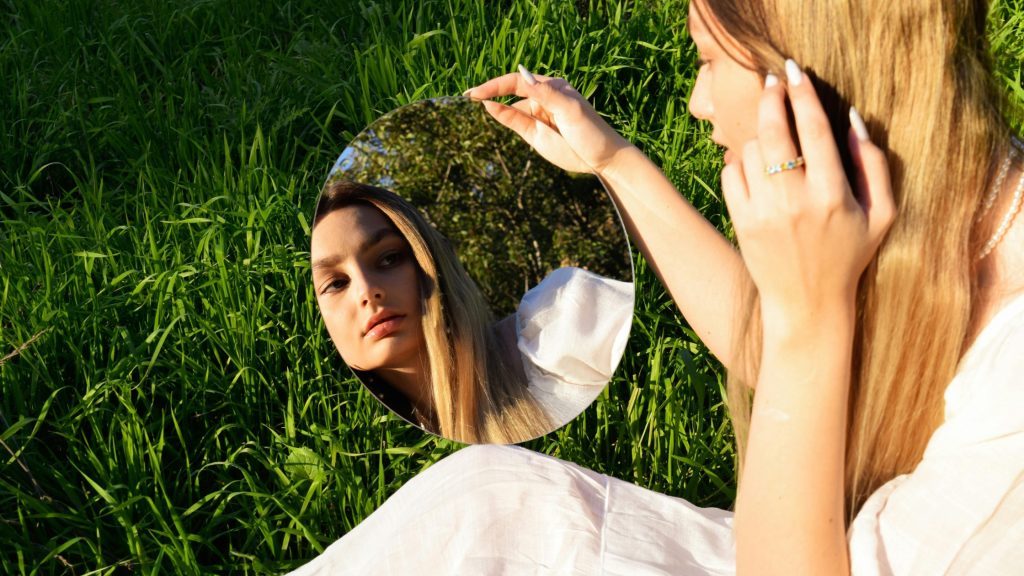 Trend beauty dopo l’estate: donna che osserva il proprio riflesso allo specchio.