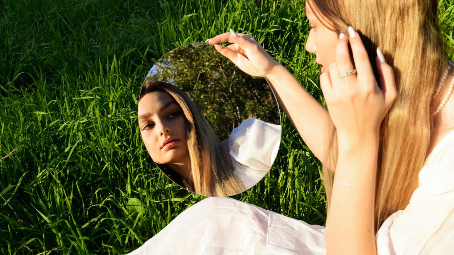 Trend beauty dopo l’estate: donna che osserva il proprio riflesso allo specchio.