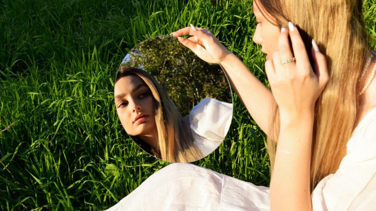 Trend beauty dopo l’estate: donna che osserva il proprio riflesso allo specchio.