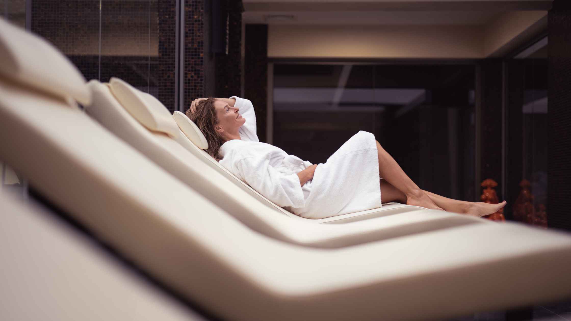 Donna che si rilassa su una chaise longue in un centro benessere durante un'esperienza spa dedicata al relax e al recupero del benessere.